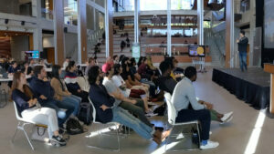 Students gathered in an atrium, listening to a guest speaker